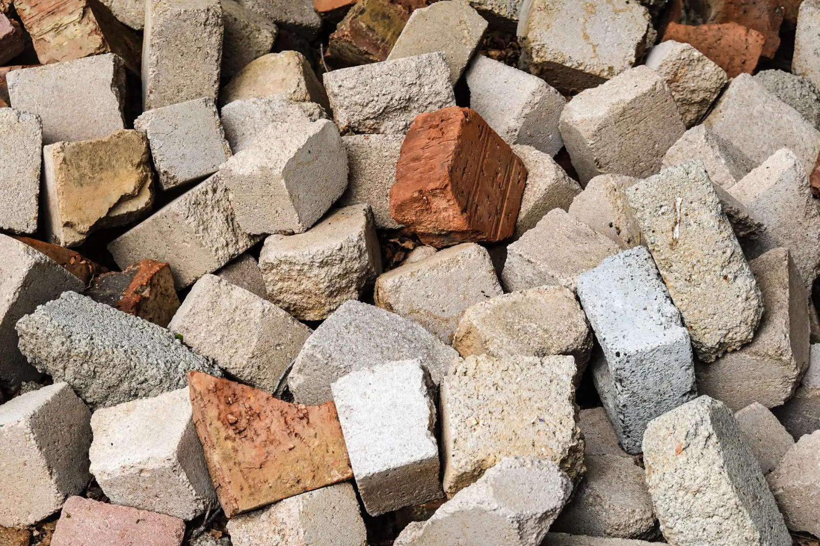 A detailed view of a rough, textured pile of concrete and clay bricks in various colors.