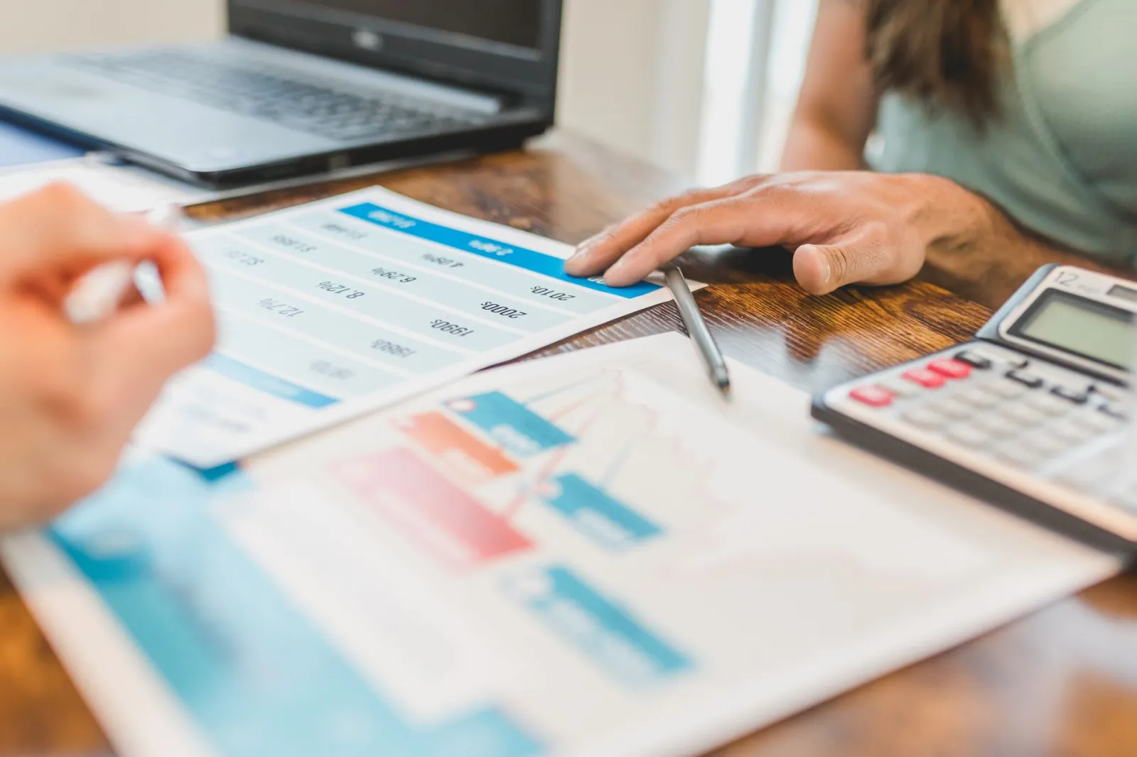 Hands at a desk with financial graphs, calculator, and pen, analyzing business data.
