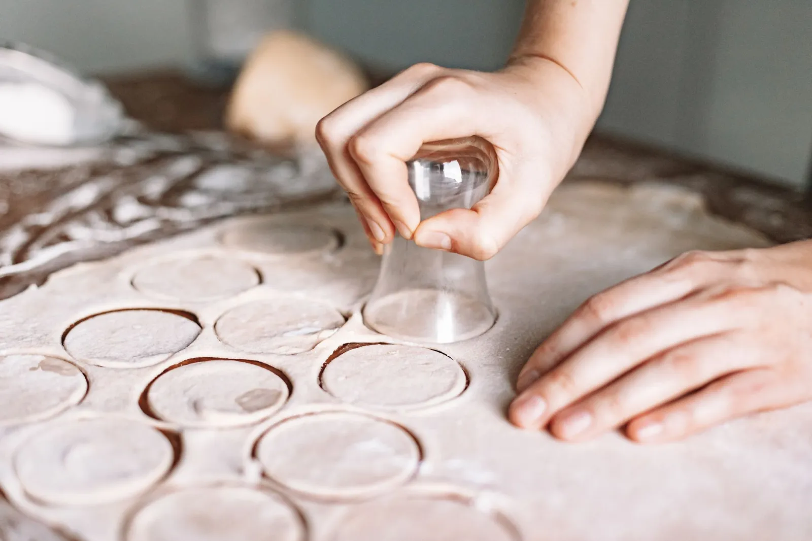 Close-up of hands cutting circles in dough, showcasing homemade food preparation.