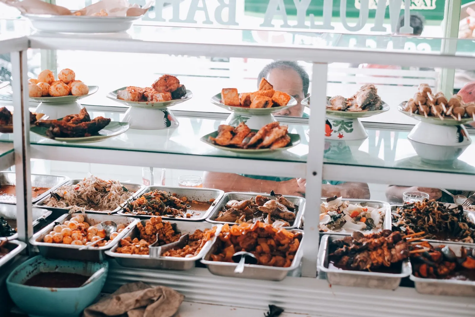 Diverse array of colorful street food dishes displayed in a glass counter at a local eatery.