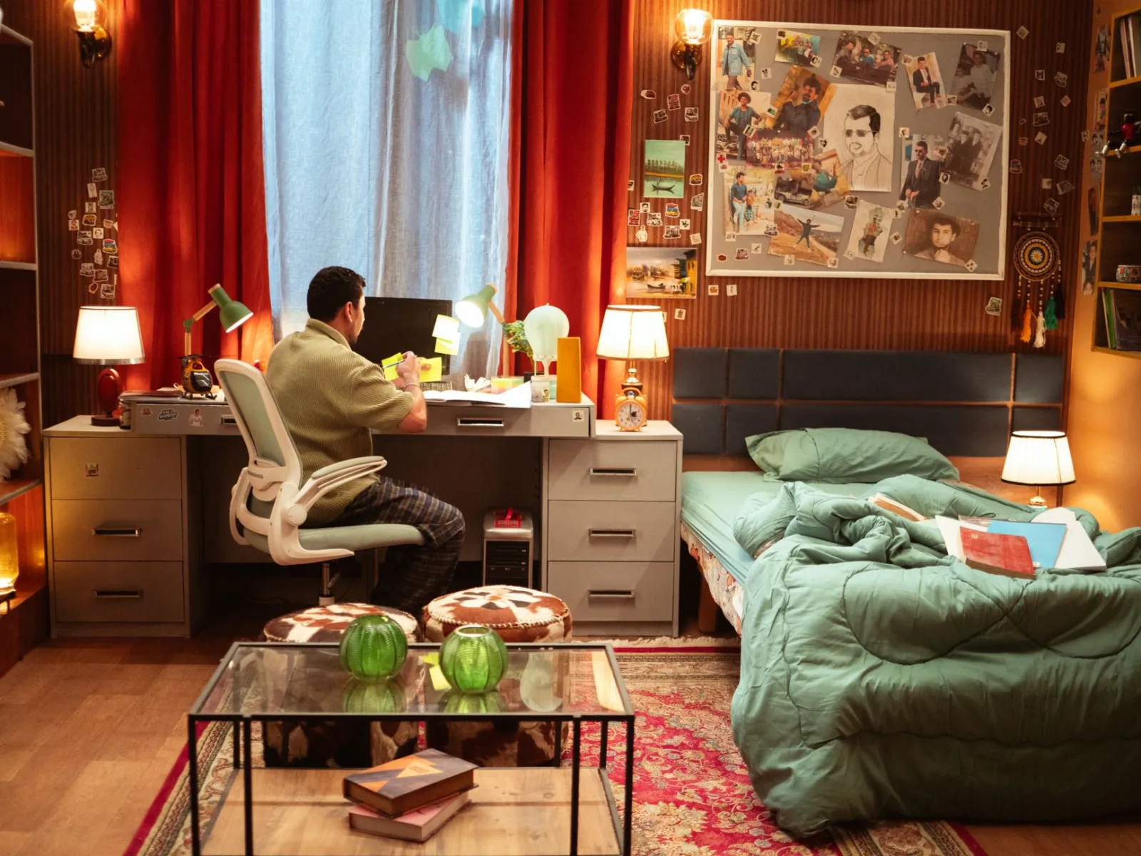A cozy bedroom with a workspace featuring warm lighting, a desk, and colorful decorations.