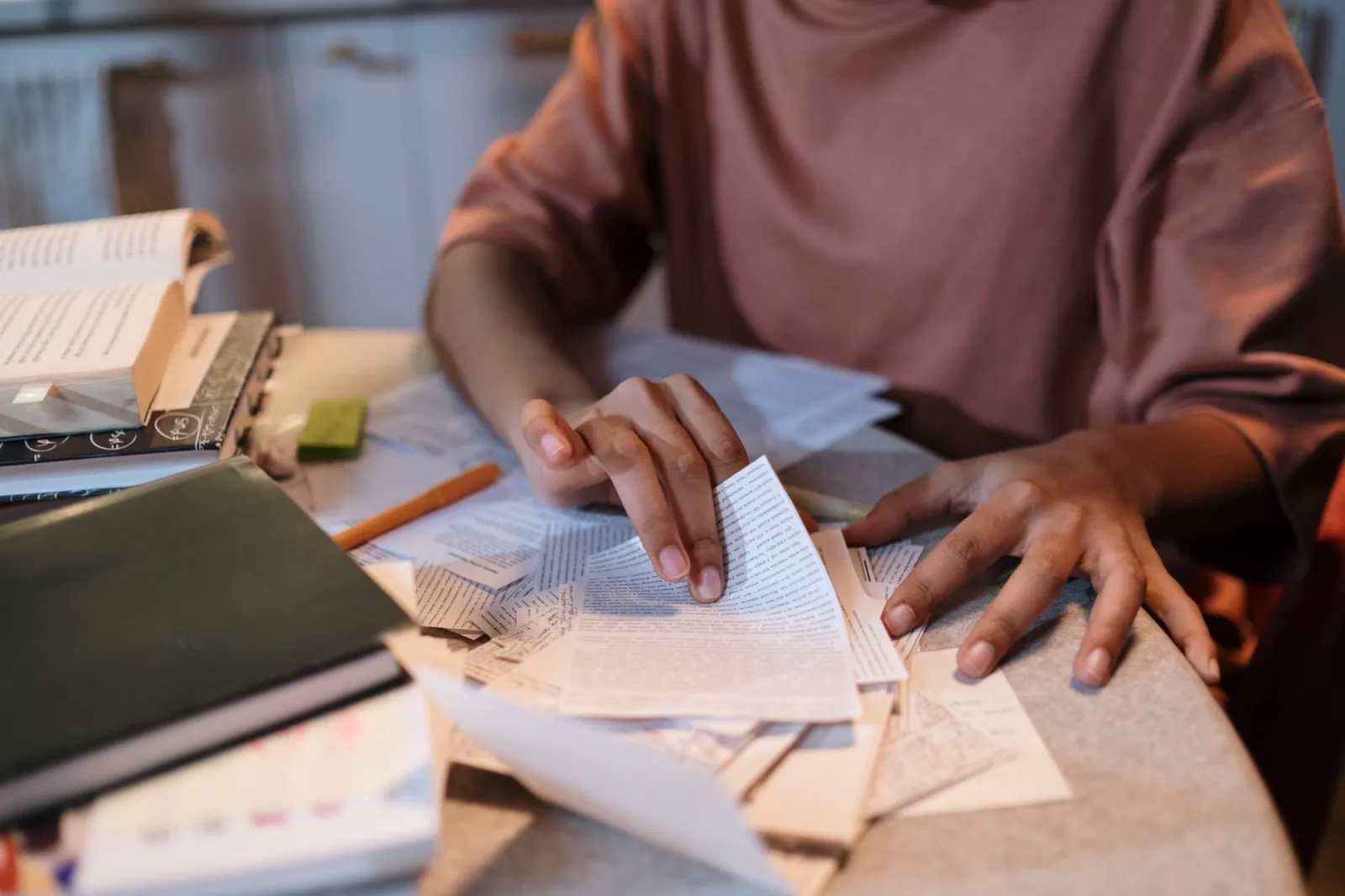 A young woman intensely studying with textbooks and notes scattered on a table.