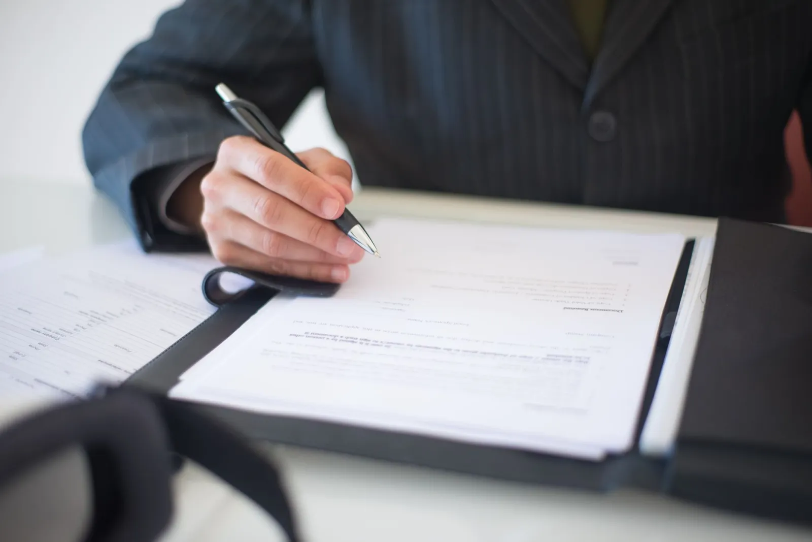 Close-up of a hand signing documents with a pen, symbolizing an important business contract.