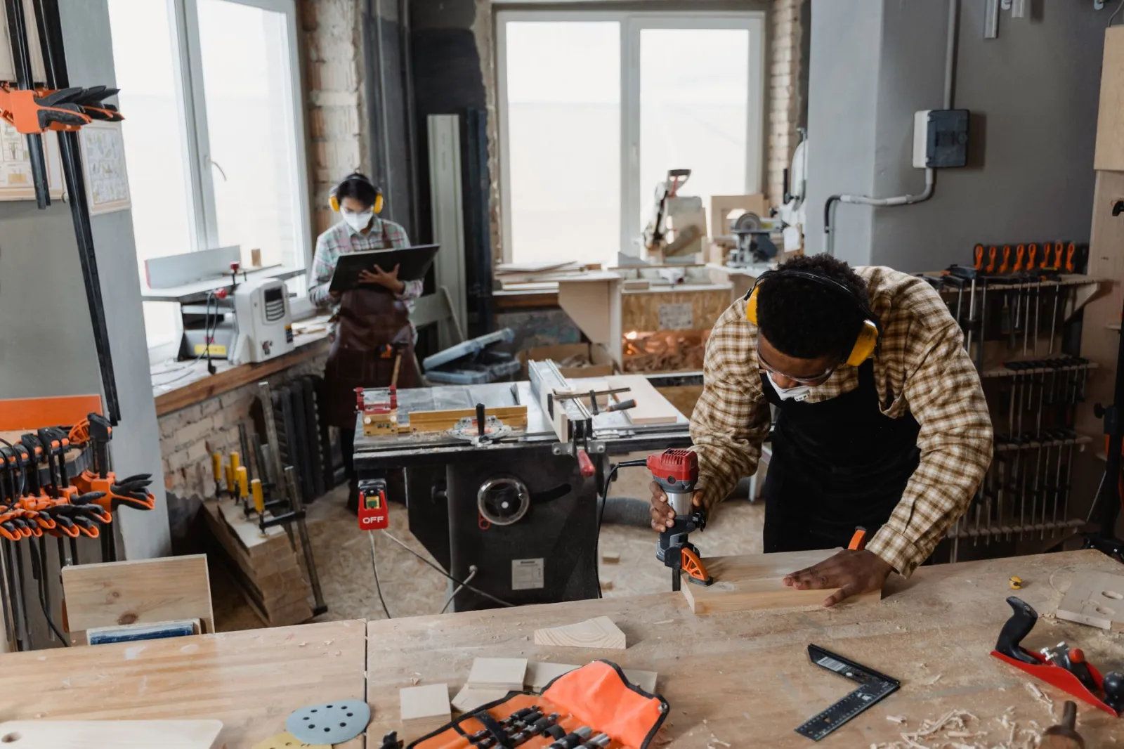 A carpenter using power tools in an indoor woodworking workshop, wearing safety gear.