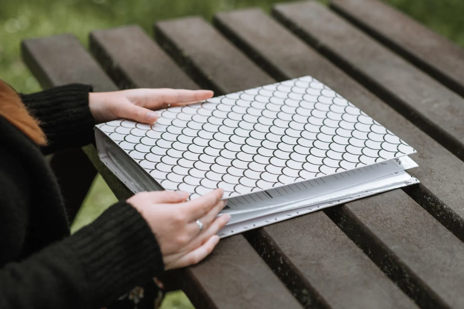 From above of female opening folder with papers on wooden bench in park
